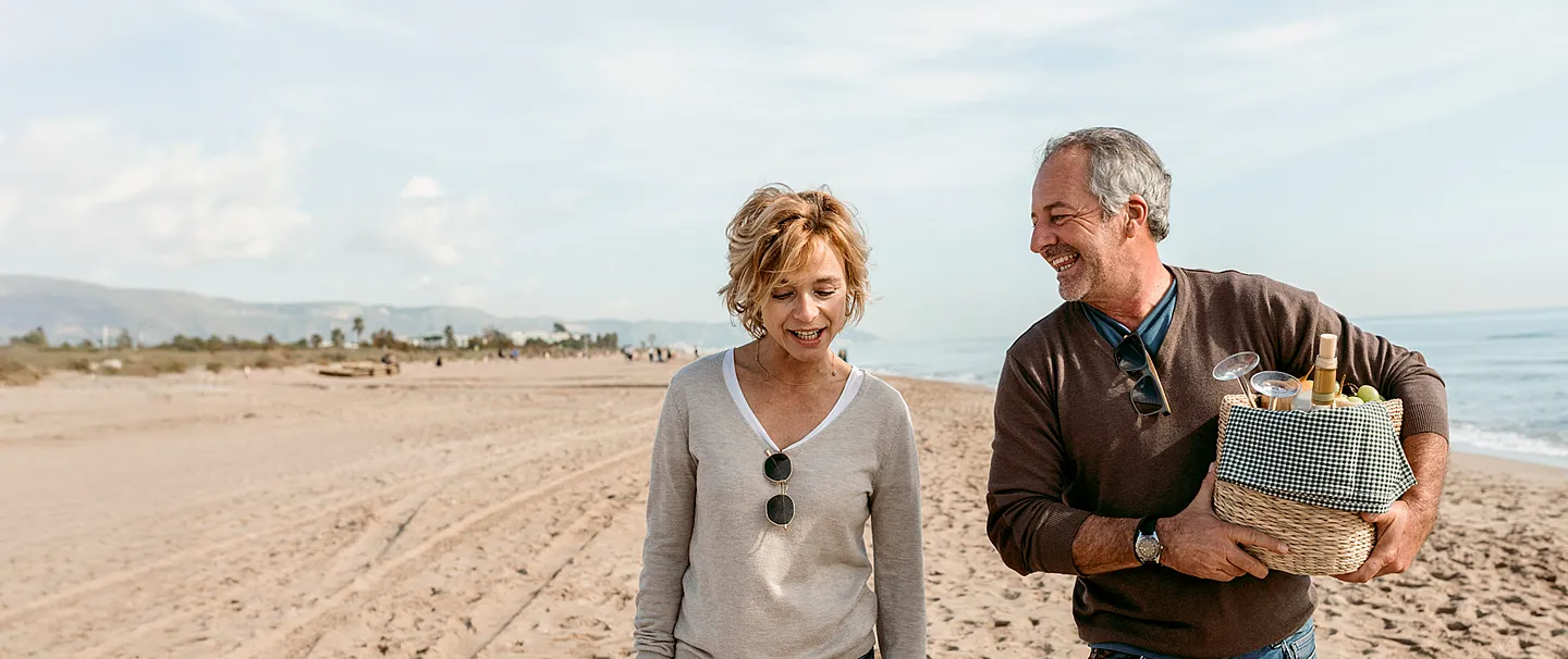 Paar, das am Strand spazieren geht und ein Picknickkörbchen hält.