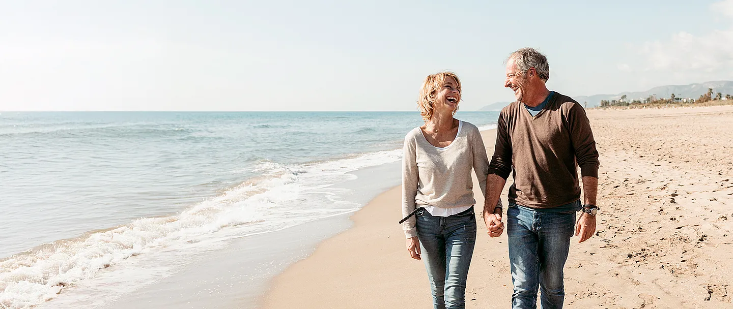 Fröhliches Paar, das barfuß am Strand läuft.